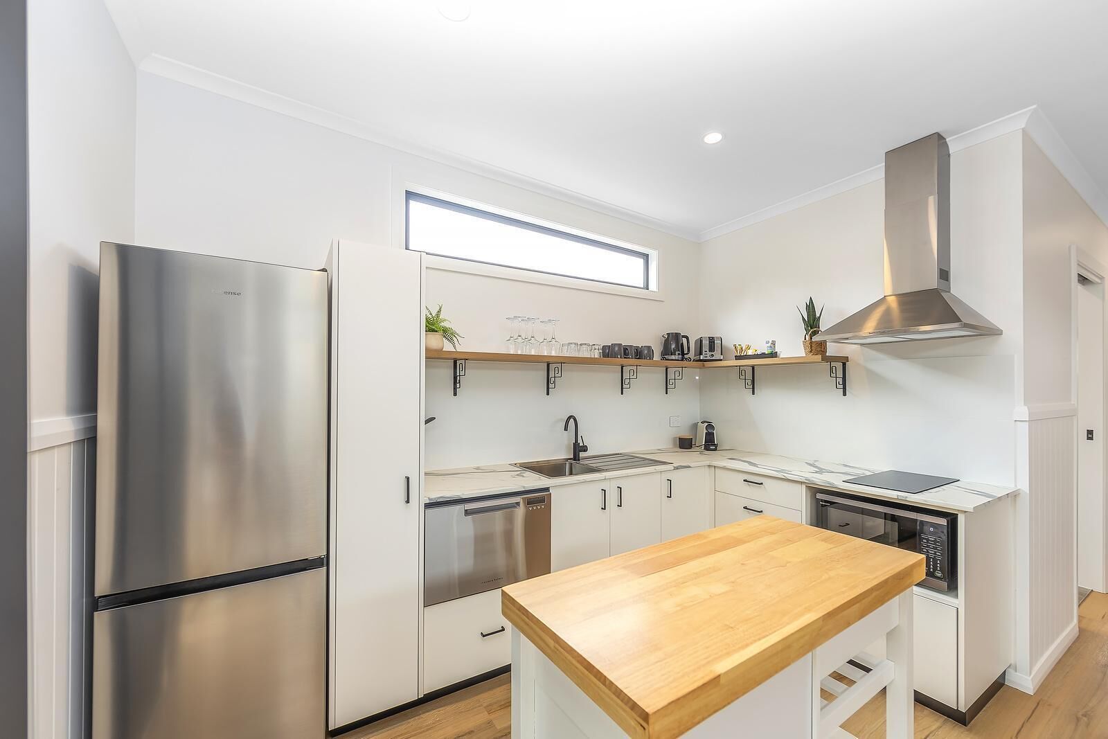 Una cocina moderna con armarios blancos, electrodomésticos de acero inoxidable y encimera de madera.