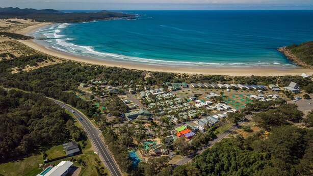 Vista aérea de un resort costero con villas frente a la playa, una piscina y un camino que lleva a la playa.