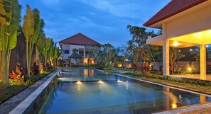 A swimming pool with a clear view of the surrounding architecture, including a building with a red roof and a well-lit outdoor area. - Taman Ayu Townhouse (Denpasar)