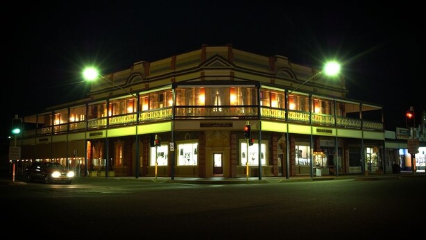 A two-story building with a balcony, illuminated by streetlights, and a car parked in front. - The Astra Hotel (Broken Hill)
