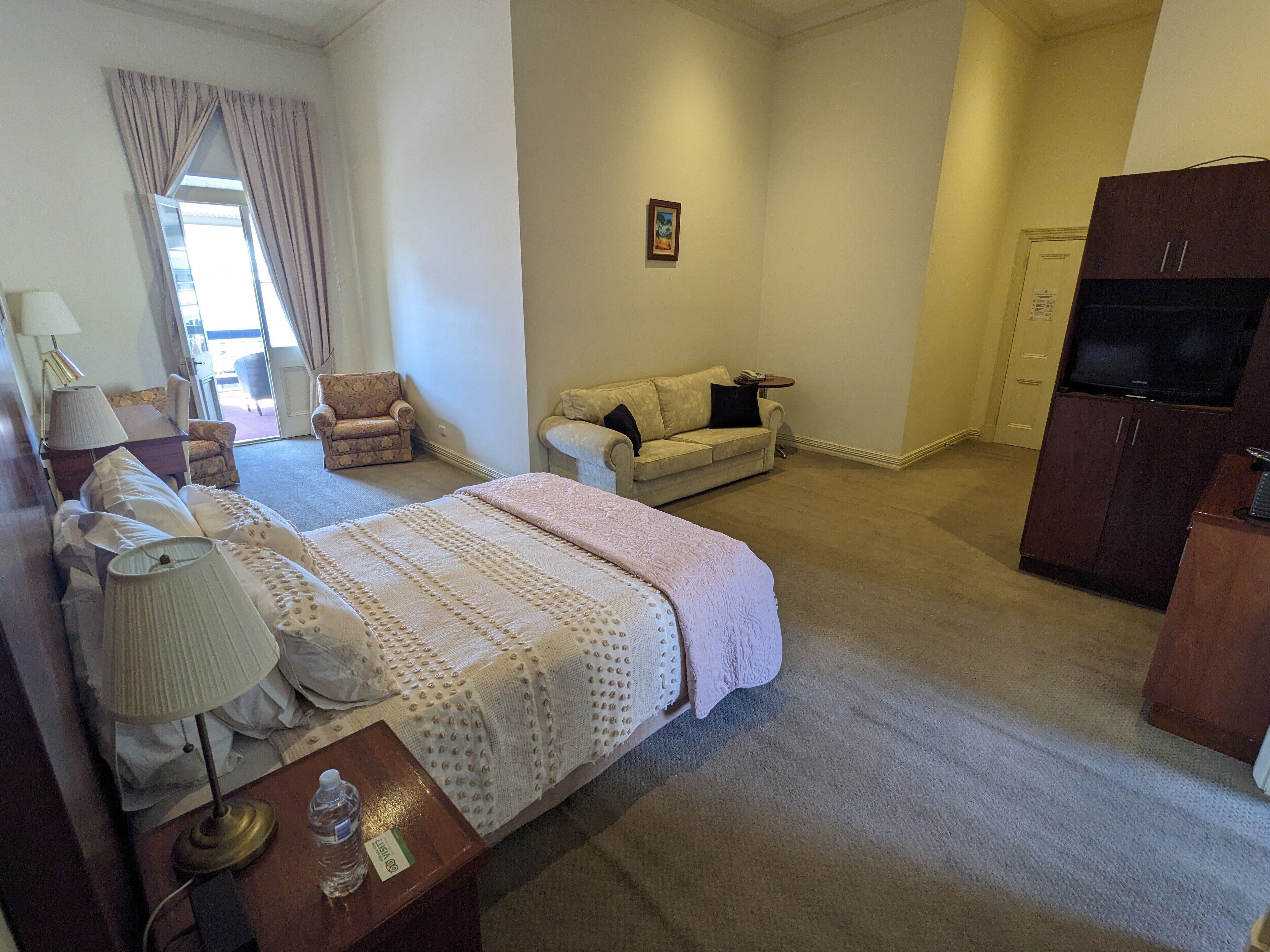 Quarto de hotel com cama, escrivaninha, poltrona, sofá, televisão e guarda-roupa.