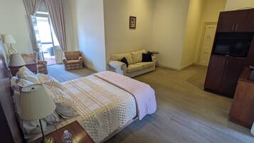 Quarto de hotel com cama, escrivaninha, poltrona, sofá, televisão e guarda-roupa.