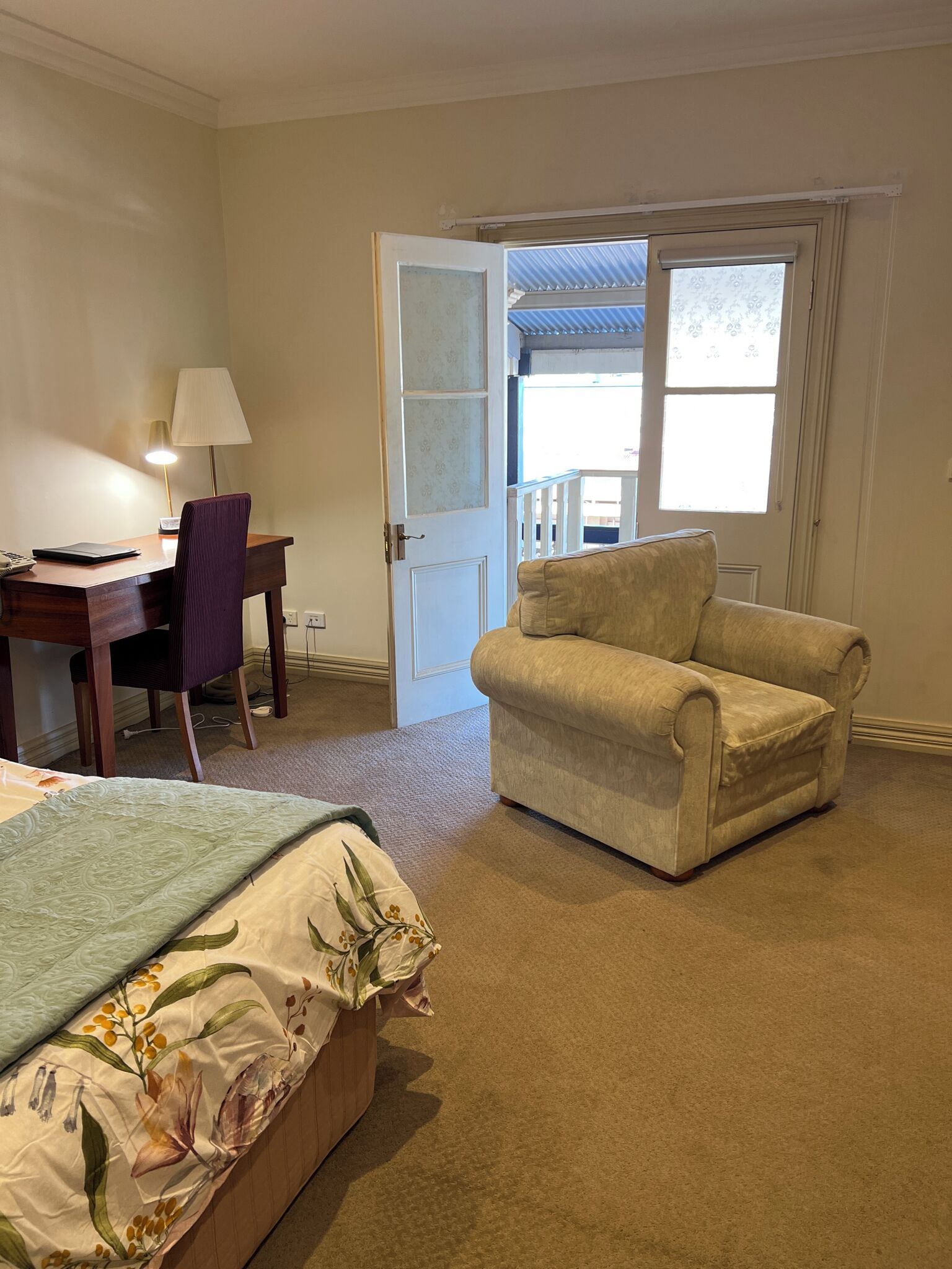 A hotel room with a bed, a desk with a lamp, a chair, and a sofa.