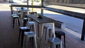 An outdoor seating area with metal tables and stools, a traffic light, and a building in the background. - The Astra Hotel (Broken Hill)