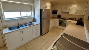 A modern kitchen with white cabinets, stainless steel appliances, a window, and a tiled floor. - The Astra Hotel (Broken Hill)