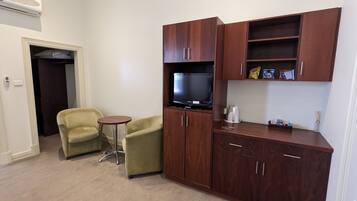 A compact room with a television, a small table, two chairs, and wooden cabinets.