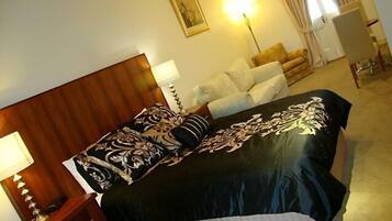 A hotel room with a large bed, a bedside table with a lamp, a chair, and a desk.