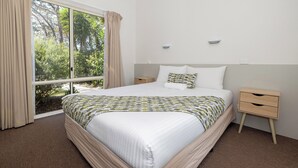 Une chambre avec un grand lit, une table de chevet, une commode et une vue sur la verdure grâce à une porte coulissante.