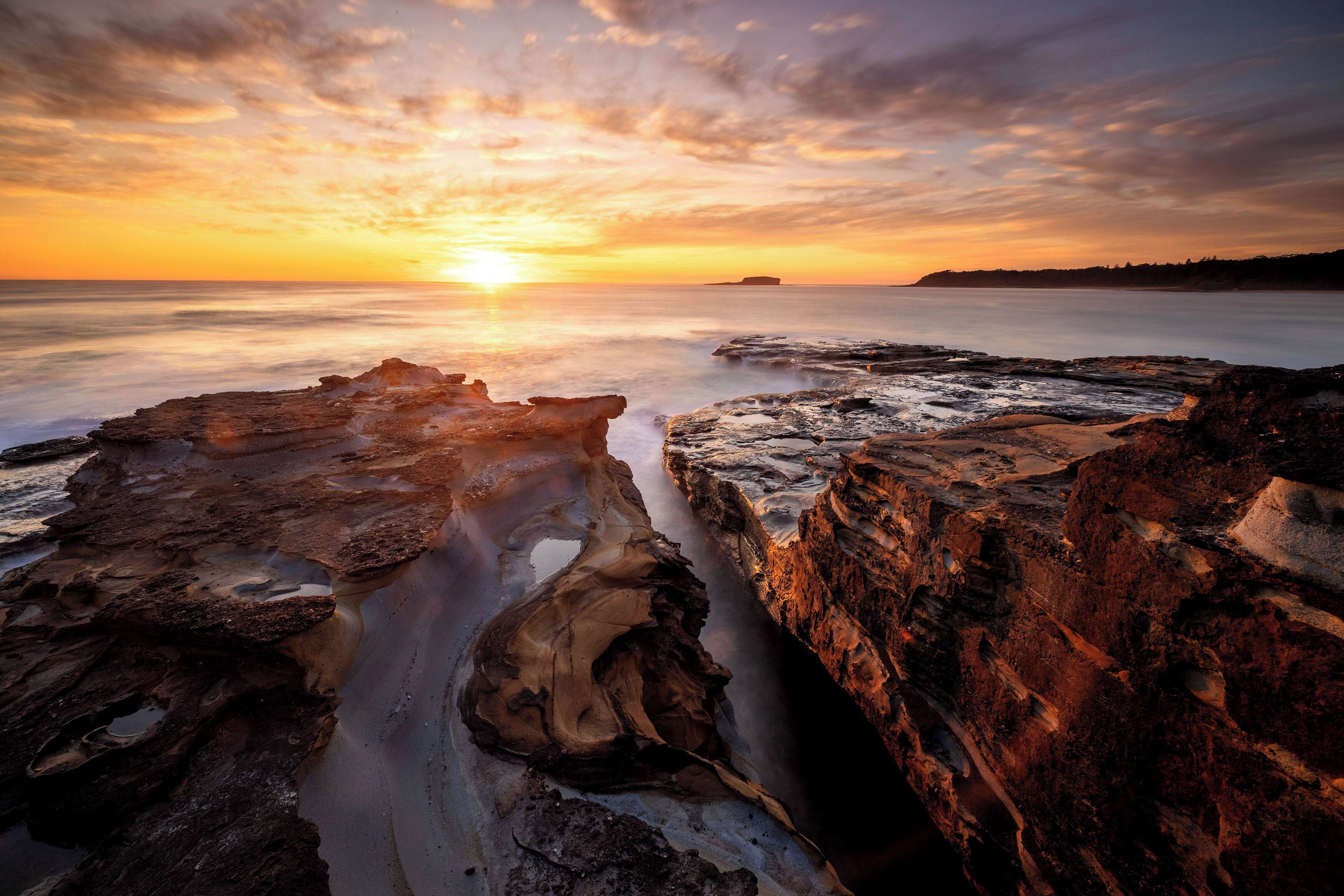 A coastal landscape with rocky formations and a sunset.