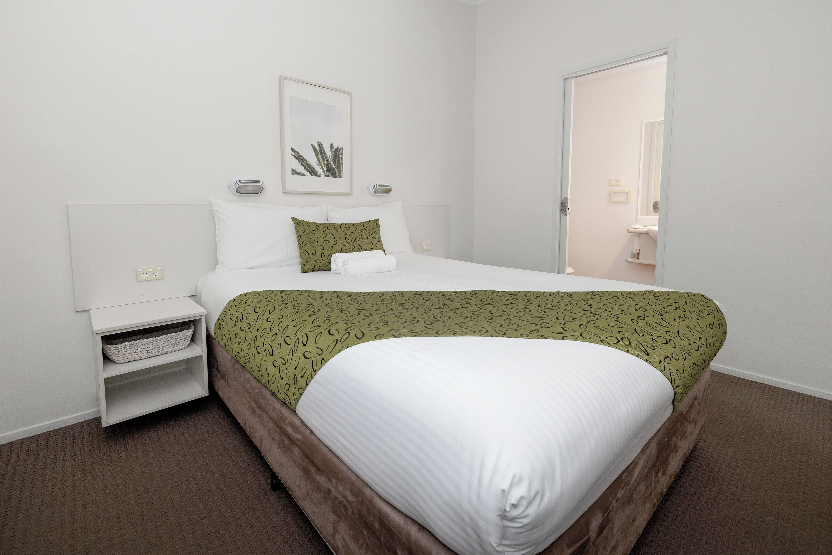 A neatly arranged hotel room with a bed, bedside table, and a small shelf.