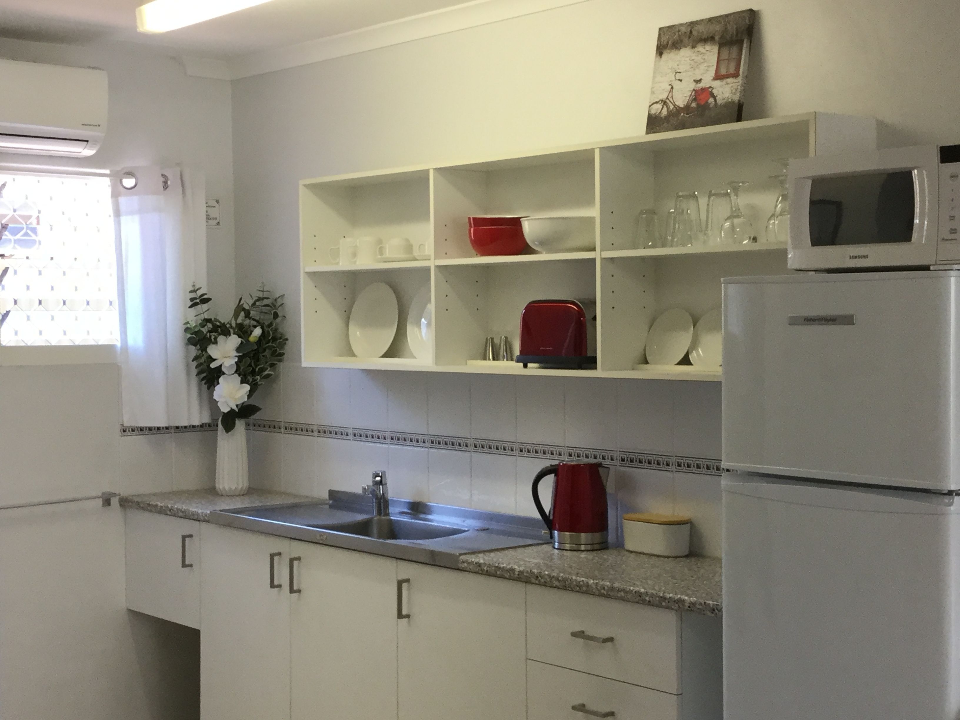 A kitchen with white cabinets, a stainless steel sink, a red kettle, and a microwave on the countertop.