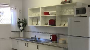 A kitchen with white cabinets, a stainless steel sink, a red kettle, and a microwave on the countertop.