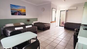 A hotel room with a bed, a desk, a chair, a ceiling fan, a clock, and a painting on the wall.