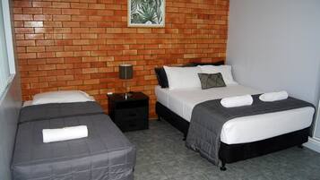 Une chambre d’hôtel avec deux lits, un mur en briques, une plante décorative dans un cadre et une table de chevet avec une lampe.