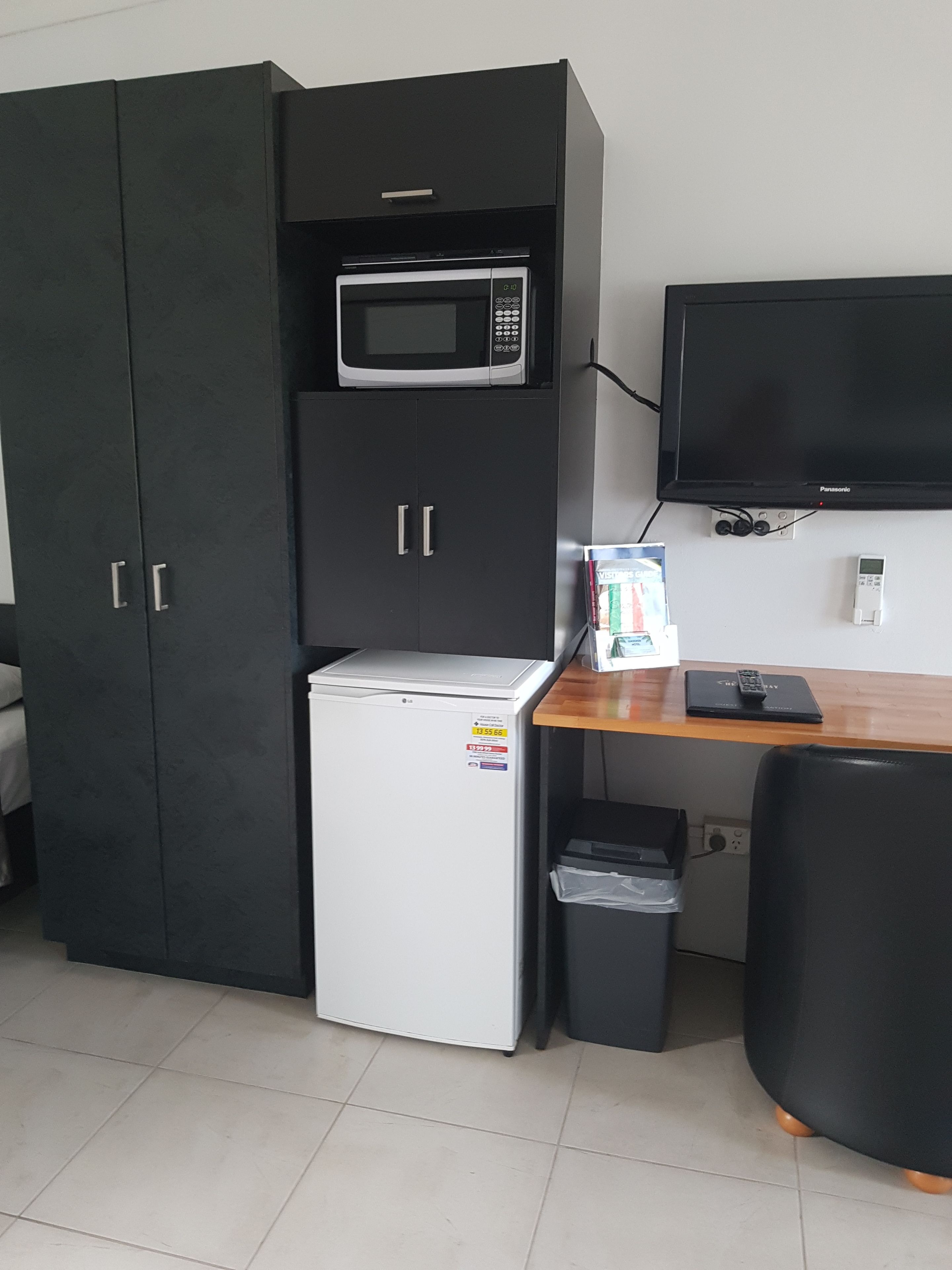Una kitchenette compacta con microondas, refrigerador y un pequeño cubo de basura.