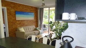 A modern kitchen with a dark countertop, a coffee machine, and a tea box. There is a beige sofa and a dining table with chairs in the background. - Sunseeker Motel (Scarness)