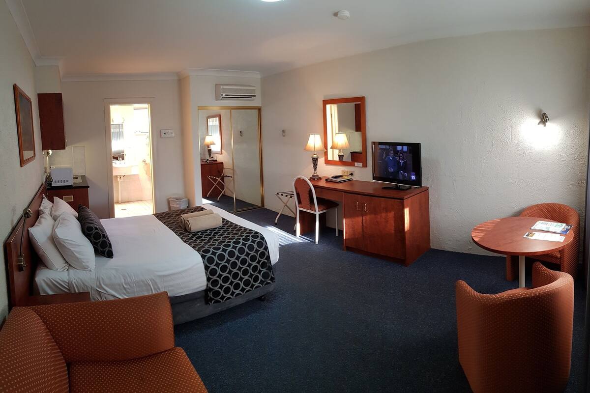 A hotel room with a bed, a desk, a TV, a chair, and a small table.