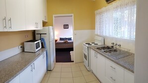 Uma cozinha compacta com armários brancos, micro-ondas, frigorífico, fogão e pia.