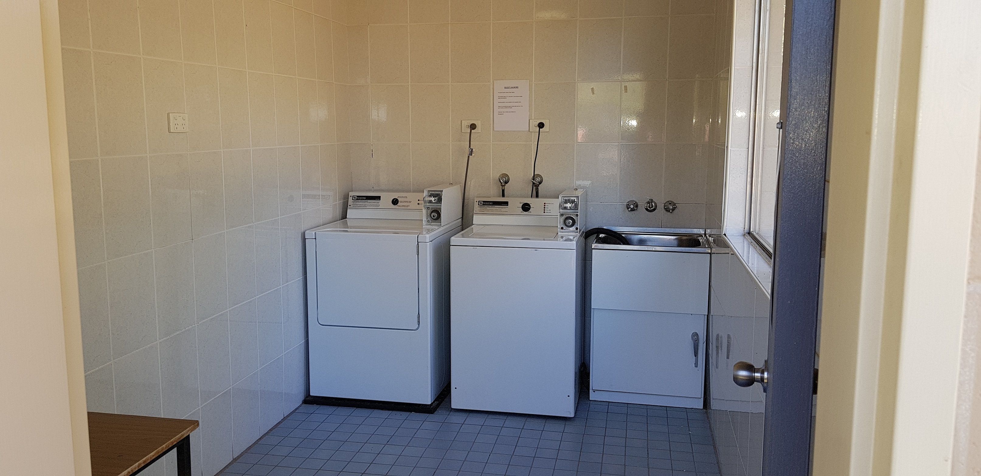 Un cuarto de lavandería con tres lavadoras y una secadora, una mesita pequeña y un lavabo.