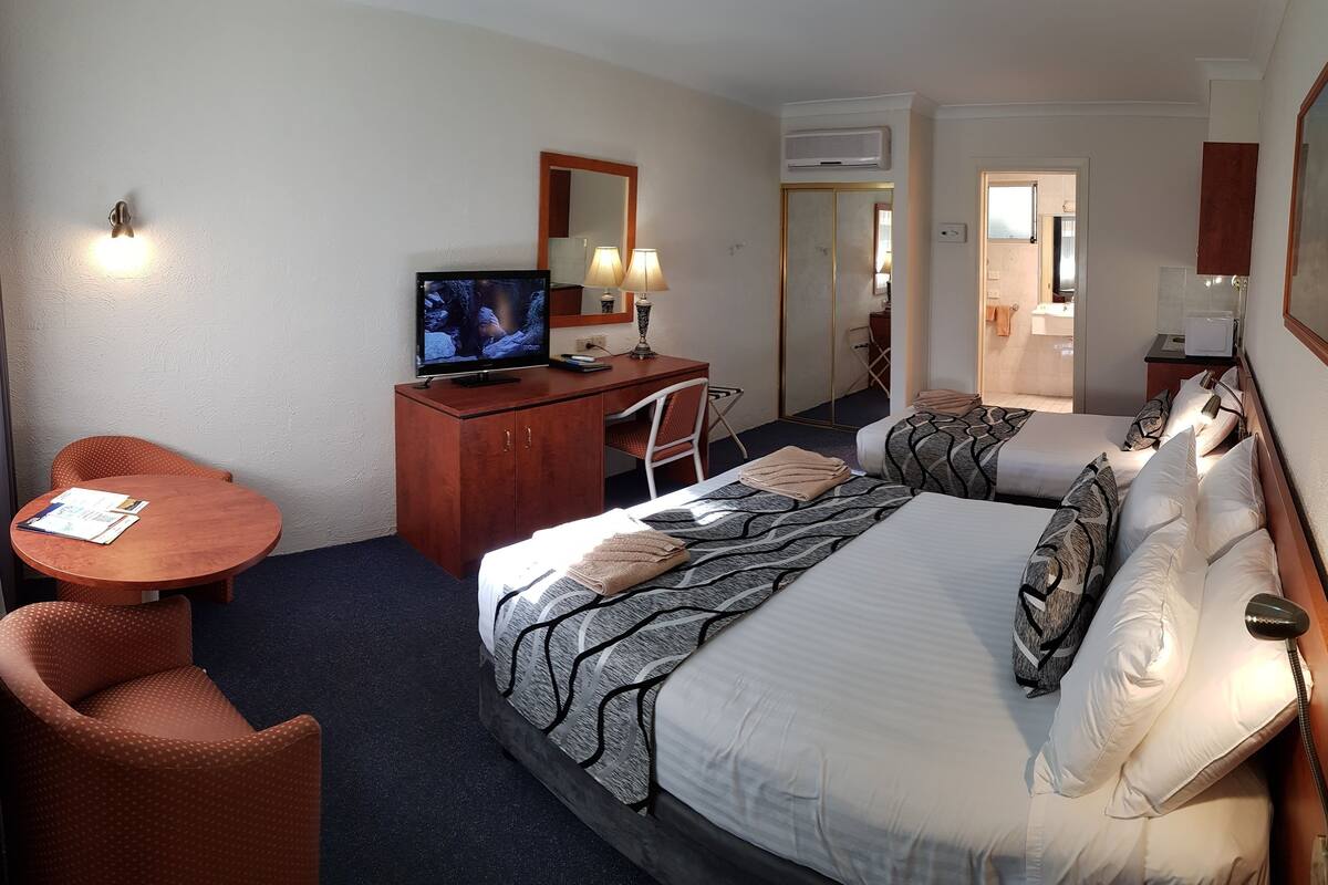 A hotel room with a bed, a desk, a chair, a television, and a bathroom visible through an open door.