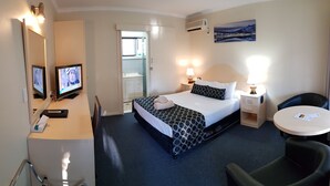 Quarto de hotel com cama, mesas de cabeceira, escrivaninha, cadeira, televisão e um quadro na parede.
