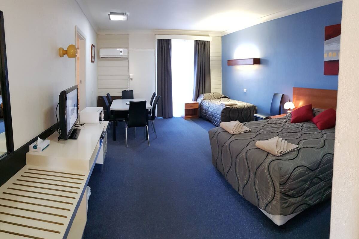 A hotel room with a bed, a desk with a chair, a small table, and a TV.