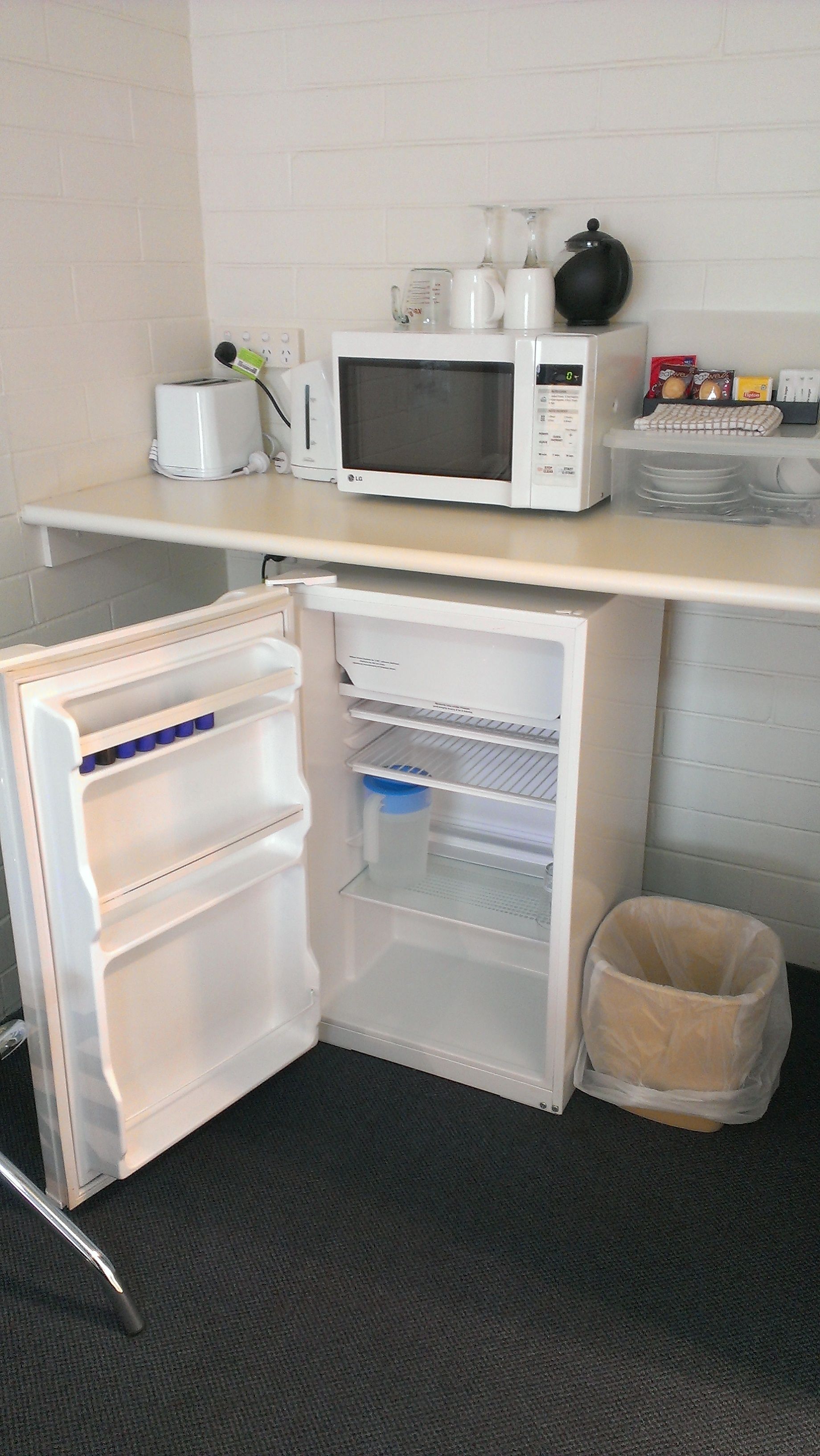 A compact kitchenette with a microwave, toaster, and a small trash bin.