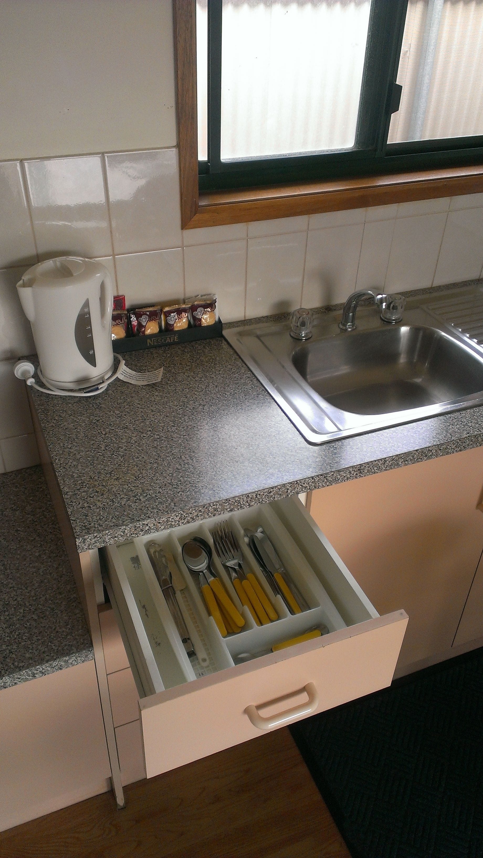 A kitchen with a granite countertop, a coffee maker, a spice rack, and a drawer with utensils.