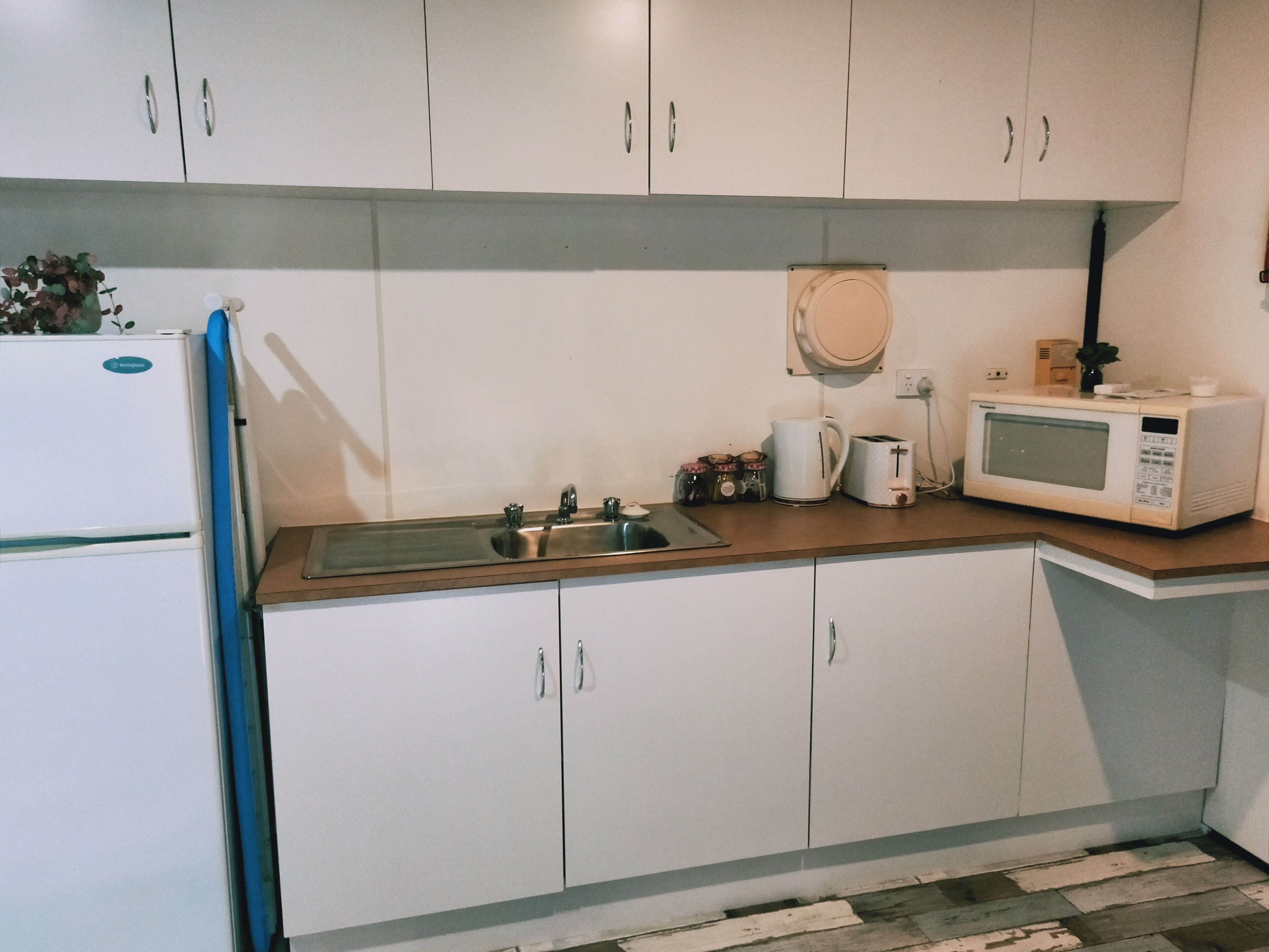 A kitchen with white cabinets, a stainless steel sink, a microwave, and a coffee maker.