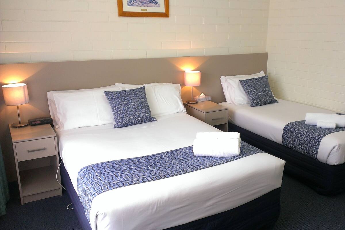 Ein Hotelzimmer mit zwei Betten, jeweils mit gemustertem Bettbezug und Kissen, einer Nachttischlampe, einem Nachttisch und einem gerahmten Bild an der Wand.