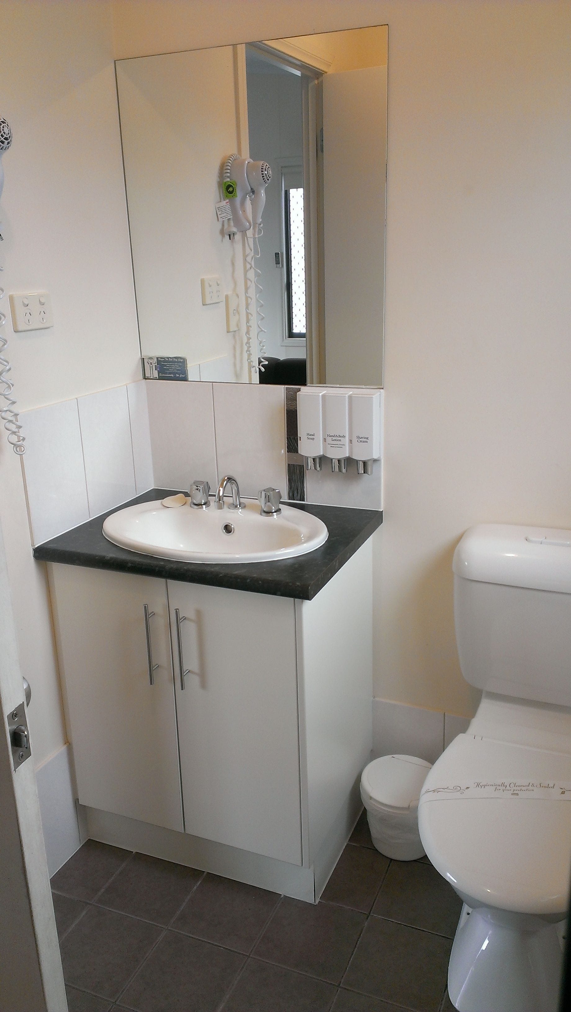 A bathroom with a white sink, a mirror, a toilet, and a hand soap dispenser.