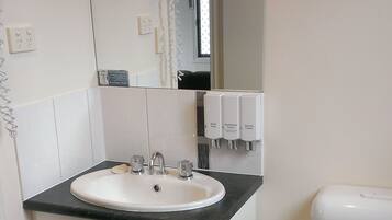 A bathroom with a white sink, a mirror, a toilet, and a hand soap dispenser.