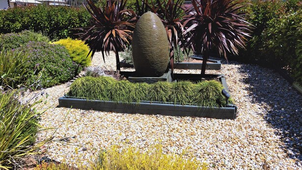 A garden with a large decorative stone, various plants, and a gravel pathway. - Oval Motel (Murray Bridge)