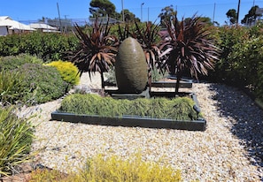 A garden with a large decorative stone, various plants, and a gravel pathway. - Oval Motel (Murray Bridge)