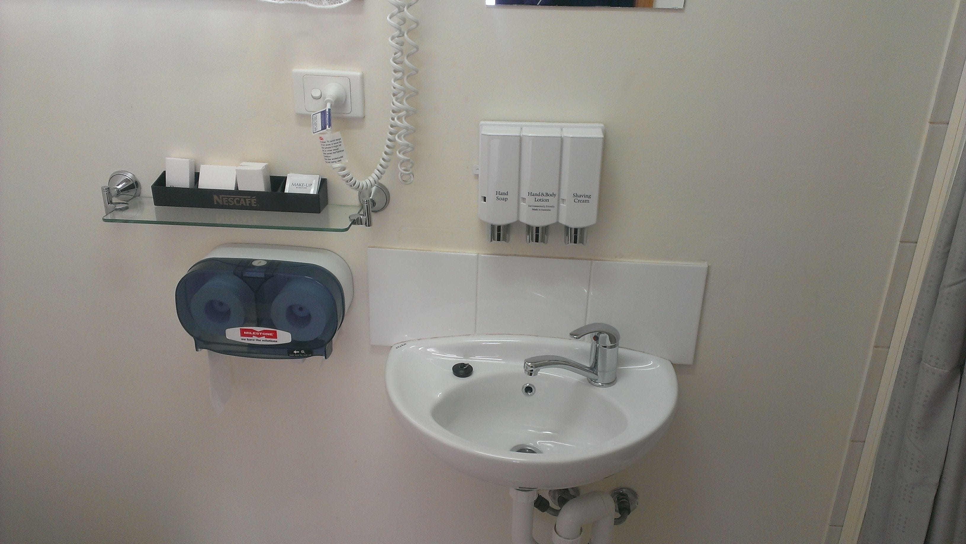 A bathroom with a sink, hand soap, lotion dispensers, and a paper towel dispenser.