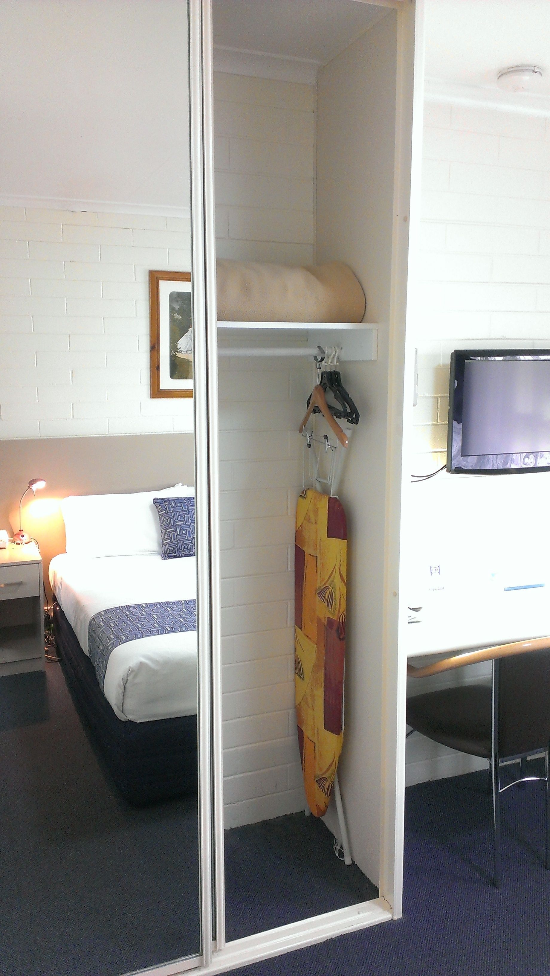 A hotel room with a bed, a desk, a television, and a coat rack with a coat.