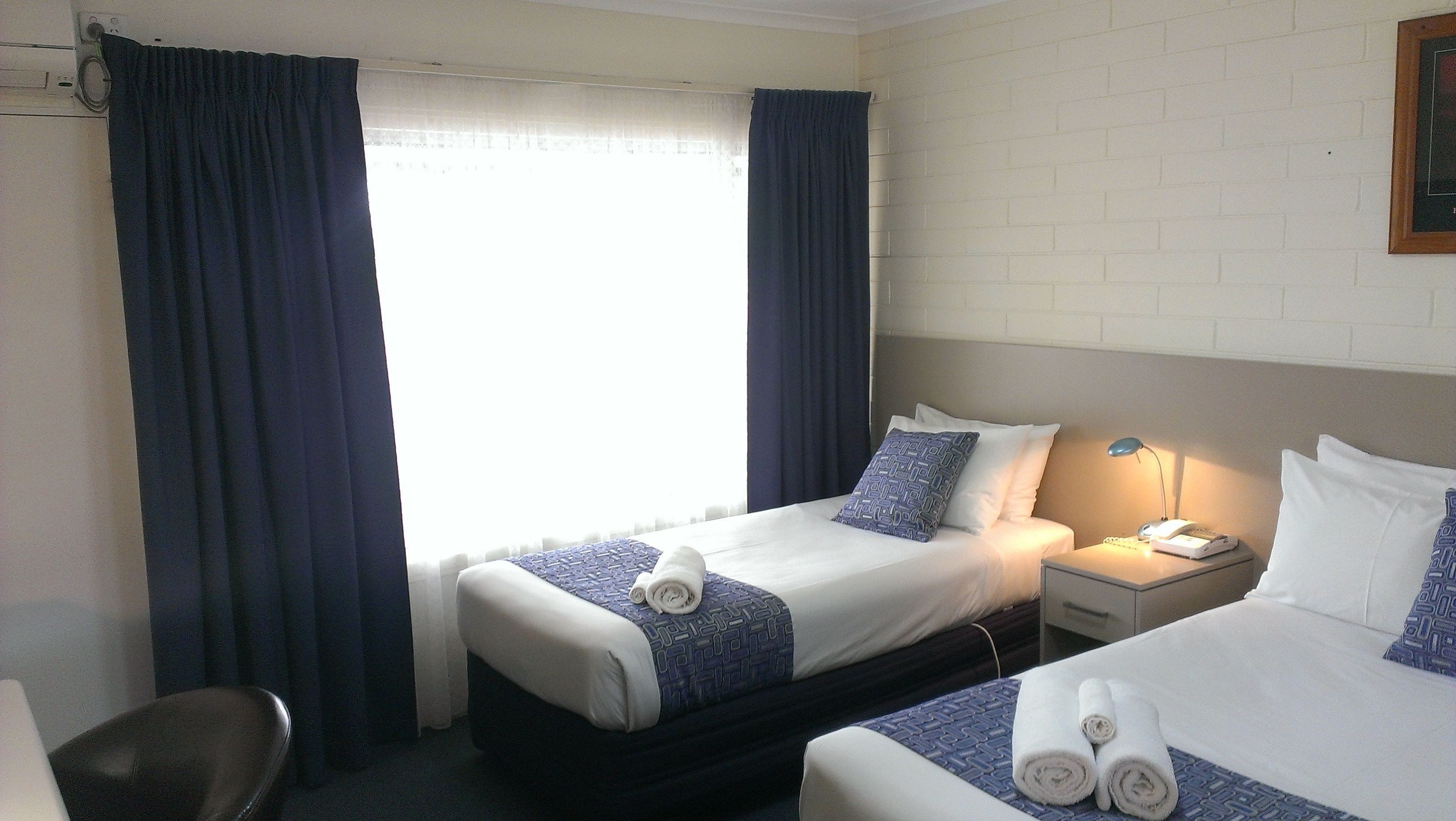 A hotel room with two beds, a desk, a chair, and a window with curtains.