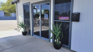 A building entrance with glass doors, a sign for keys, and two potted plants. - Oval Motel (Murray Bridge)