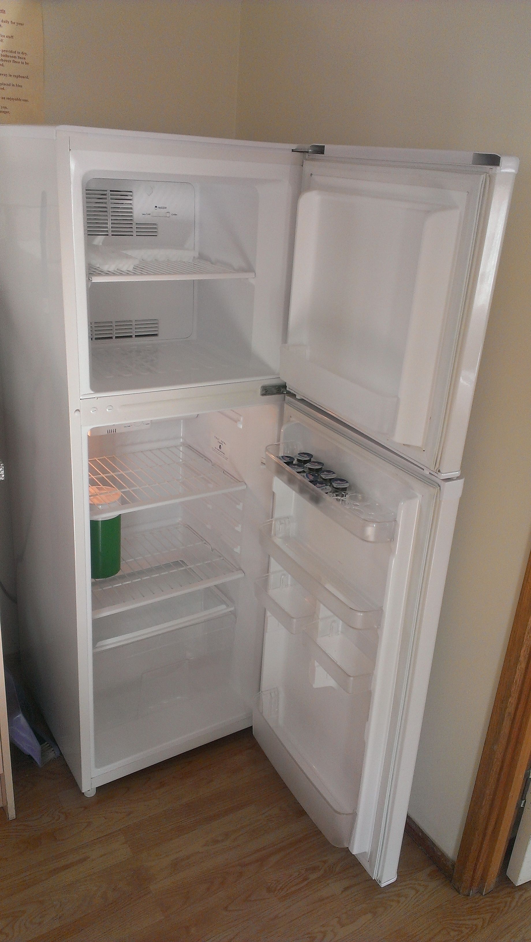 A white refrigerator with two doors, a freezer compartment, and a shelf with jars.