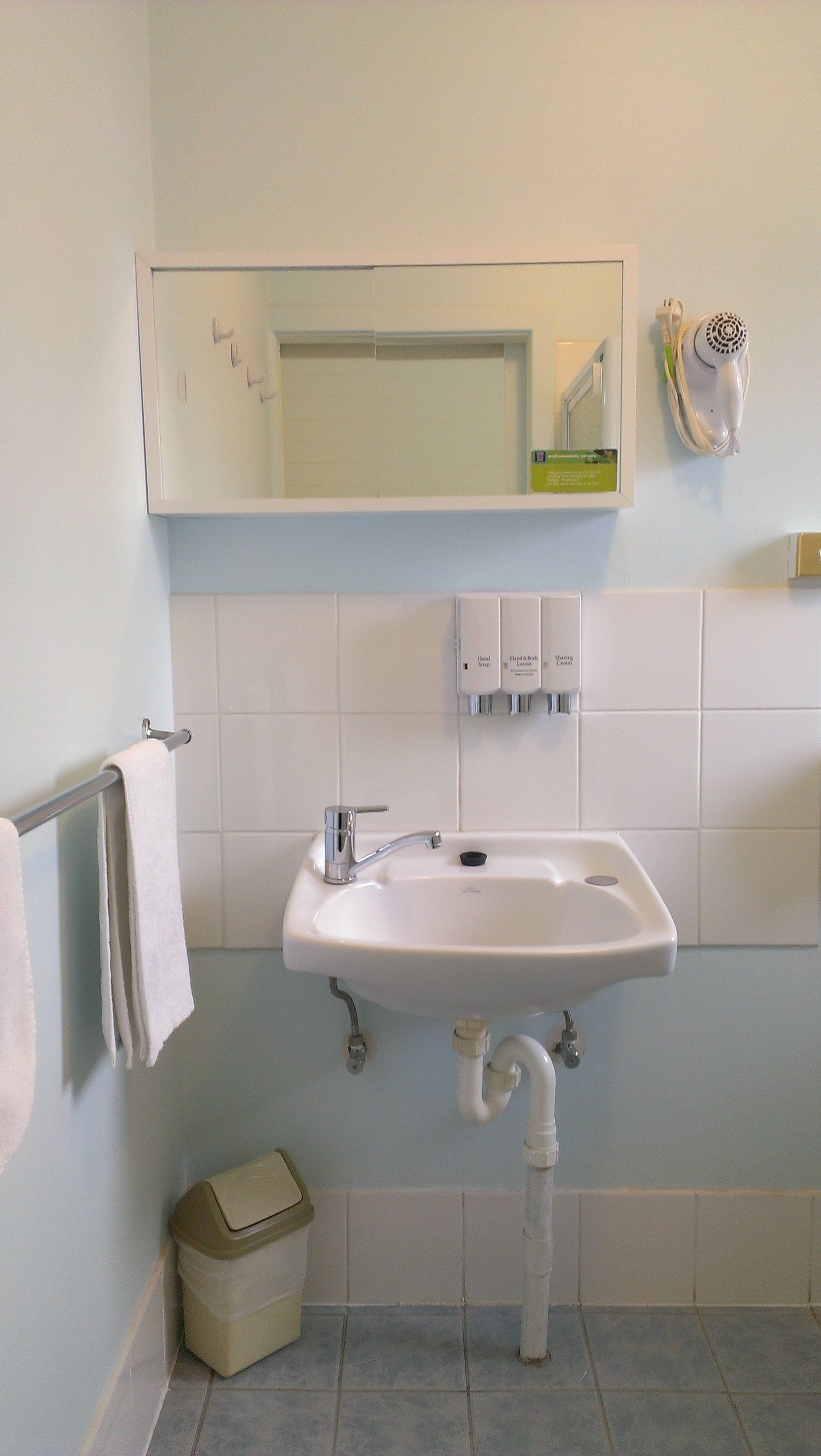 Une salle de bain avec un lavabo blanc, un miroir et des distributeurs de savon pour les mains.