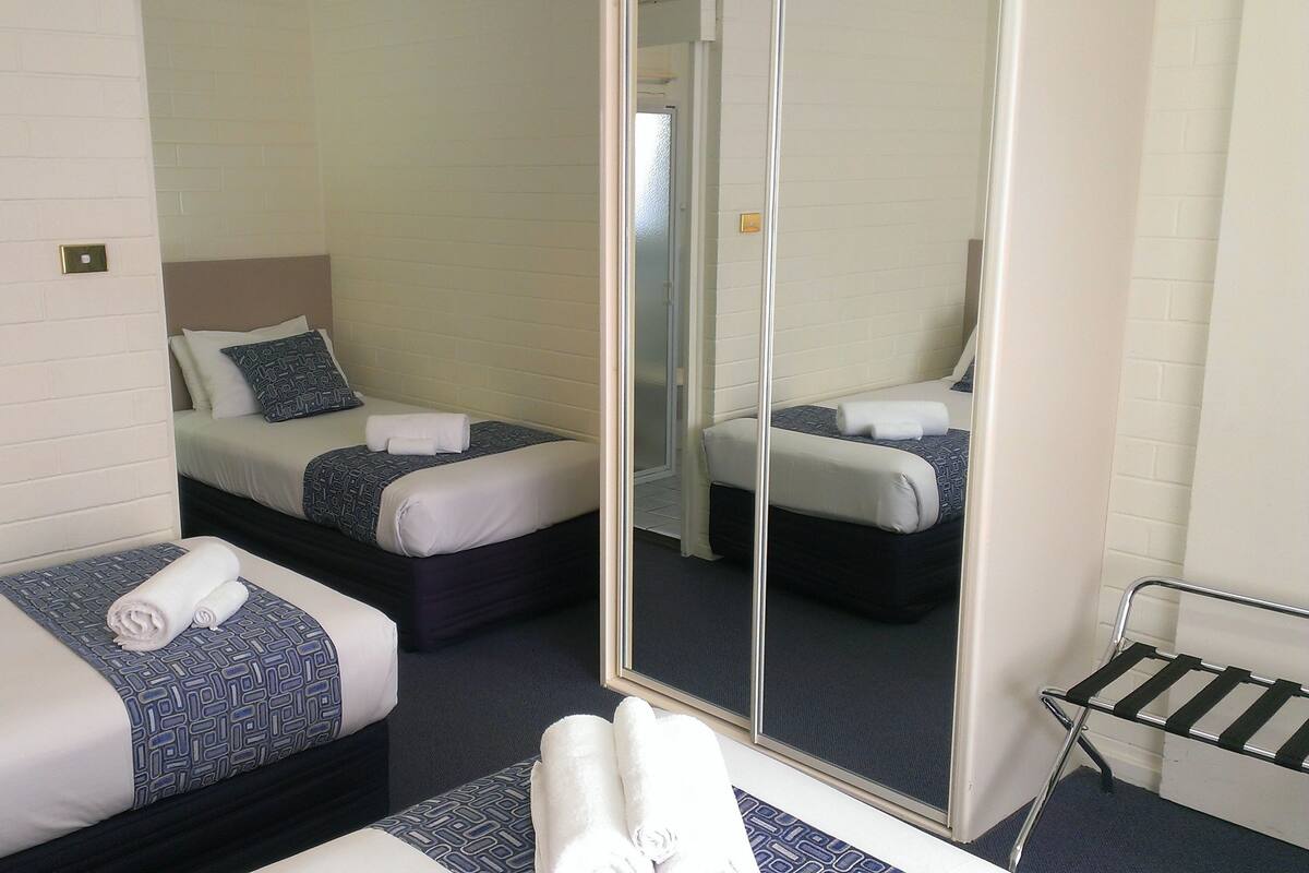 Ein Hotelzimmer mit zwei Einzelbetten, einem großen Spiegel und einer kleinen Sitzecke mit einem Metallgestell.