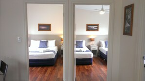 A mirrored view of a hotel room with two beds, wooden flooring, and a ceiling fan. - Oval Motel (Murray Bridge)