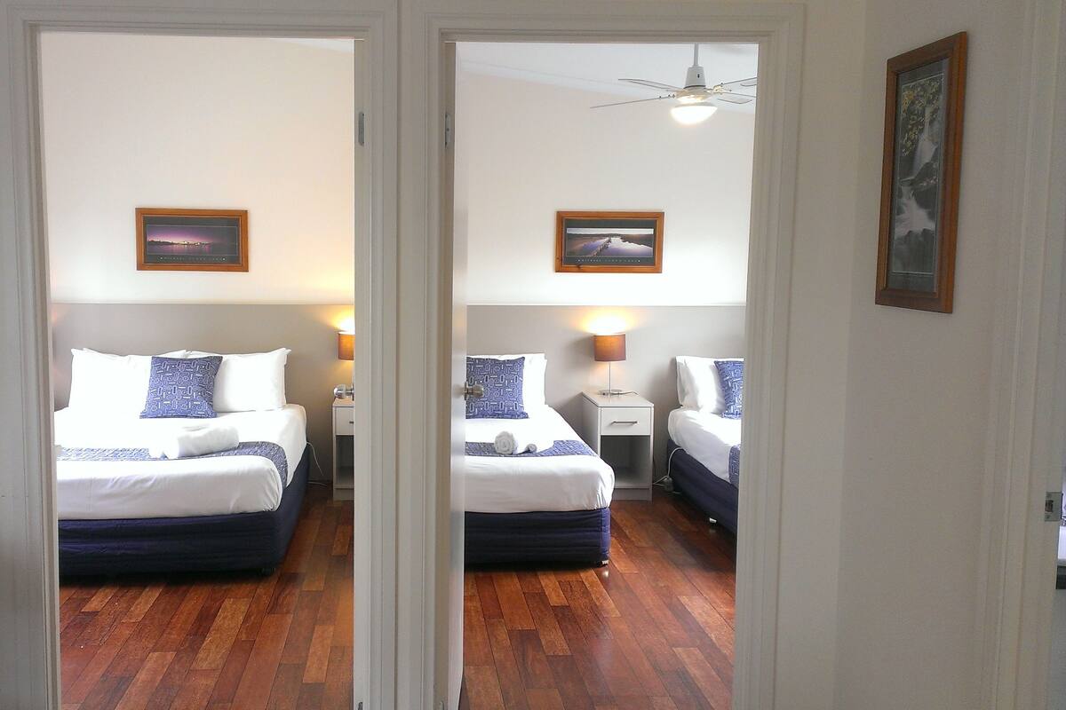 Spiegelbild eines Hotelzimmers mit zwei Betten, Holzboden und Deckenventilator.