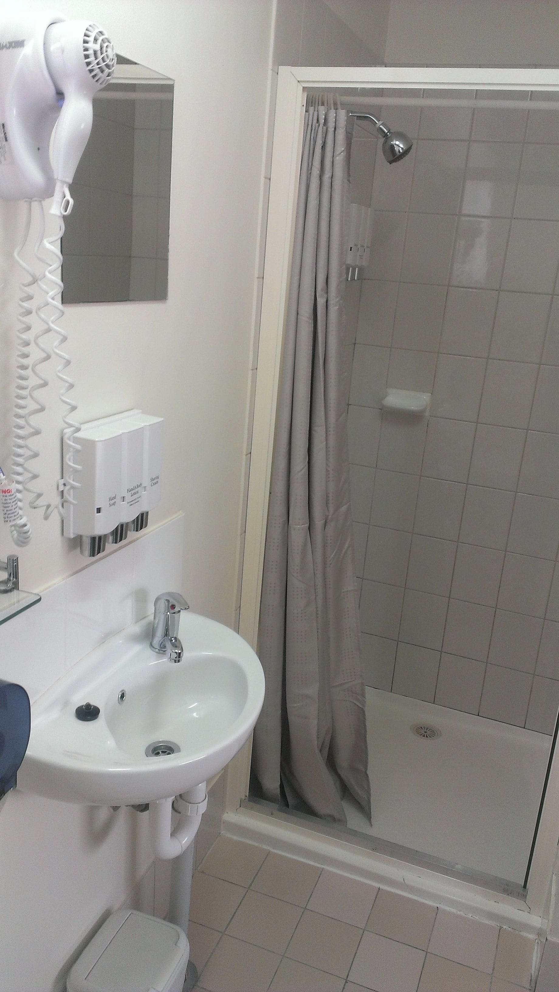 A bathroom with a sink, hand soap dispenser, and a hairdryer.