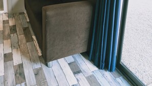 A room with a dark grey sofa, a framed abstract artwork, wooden paneling, and a large window with a curtain. - Oval Motel (Murray Bridge)