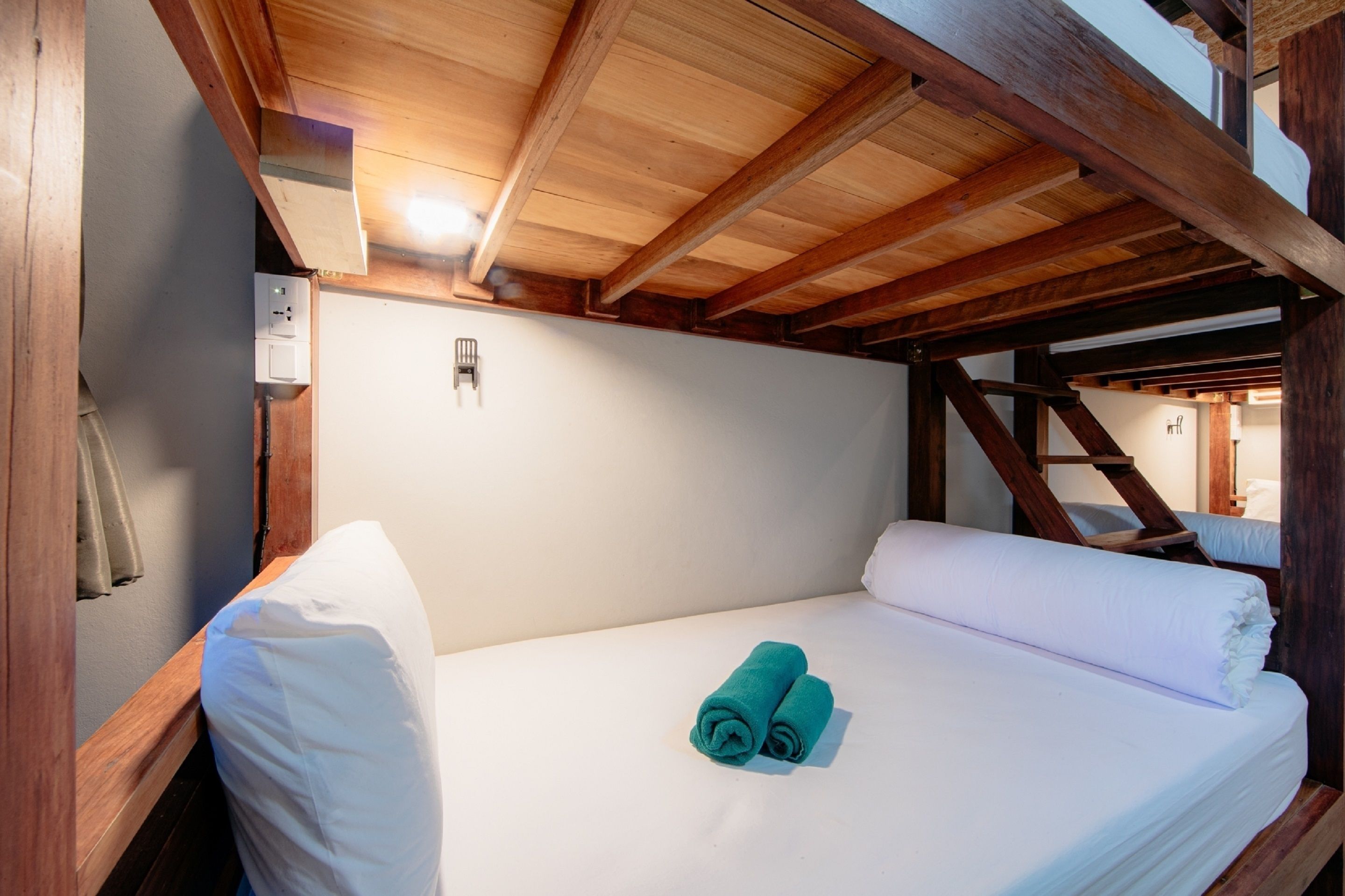 Una habitación pequeña y acogedora, con techo de madera y una cama individual con ropa de cama blanca y una toalla verde azulado.
