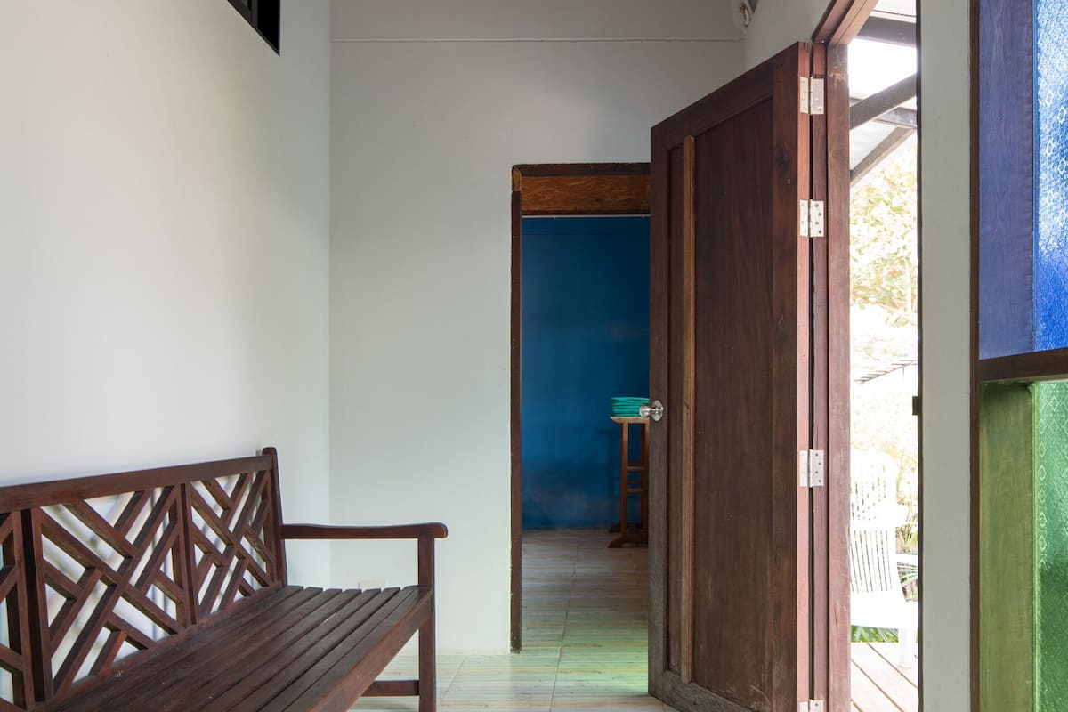 Un pasillo con un banco de madera, techo con vigas de madera y una puerta que da a otra habitación.