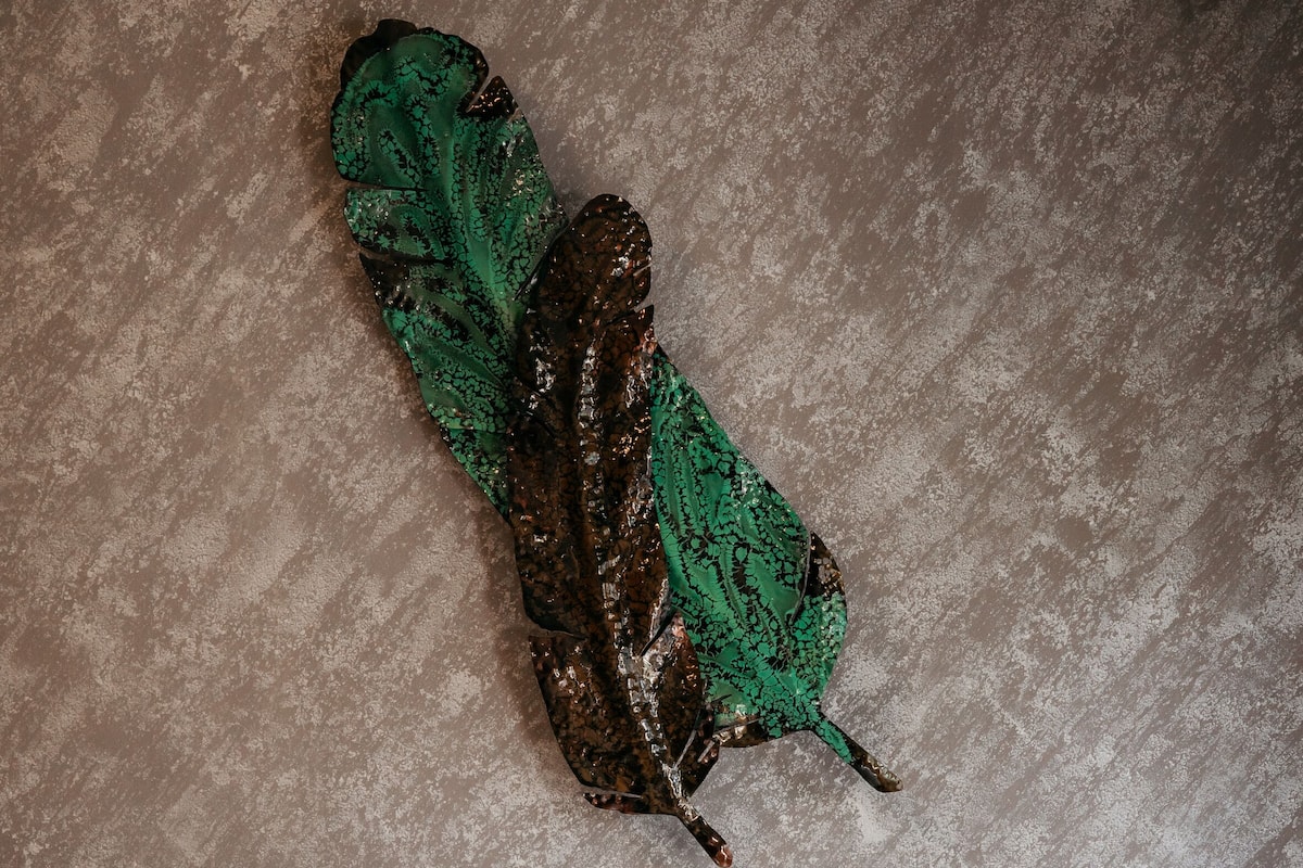 Una cama con cabecera de madera, un pequeño banco de madera y una obra de arte de una mariposa verde en la pared.
