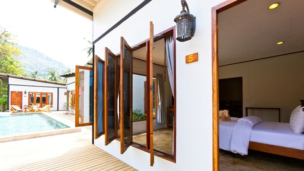A hotel room with a bed, a wooden deck, and a pool.