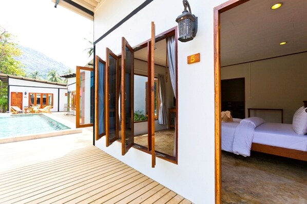 Una habitación de hotel con cama, terraza de madera y piscina.